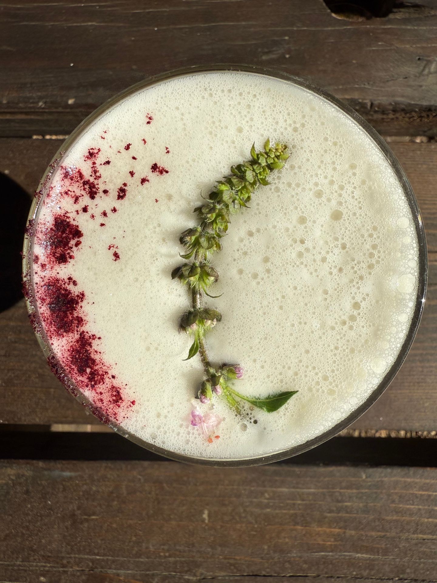 Creamy drink with flower and red textured garnish on wooden table.