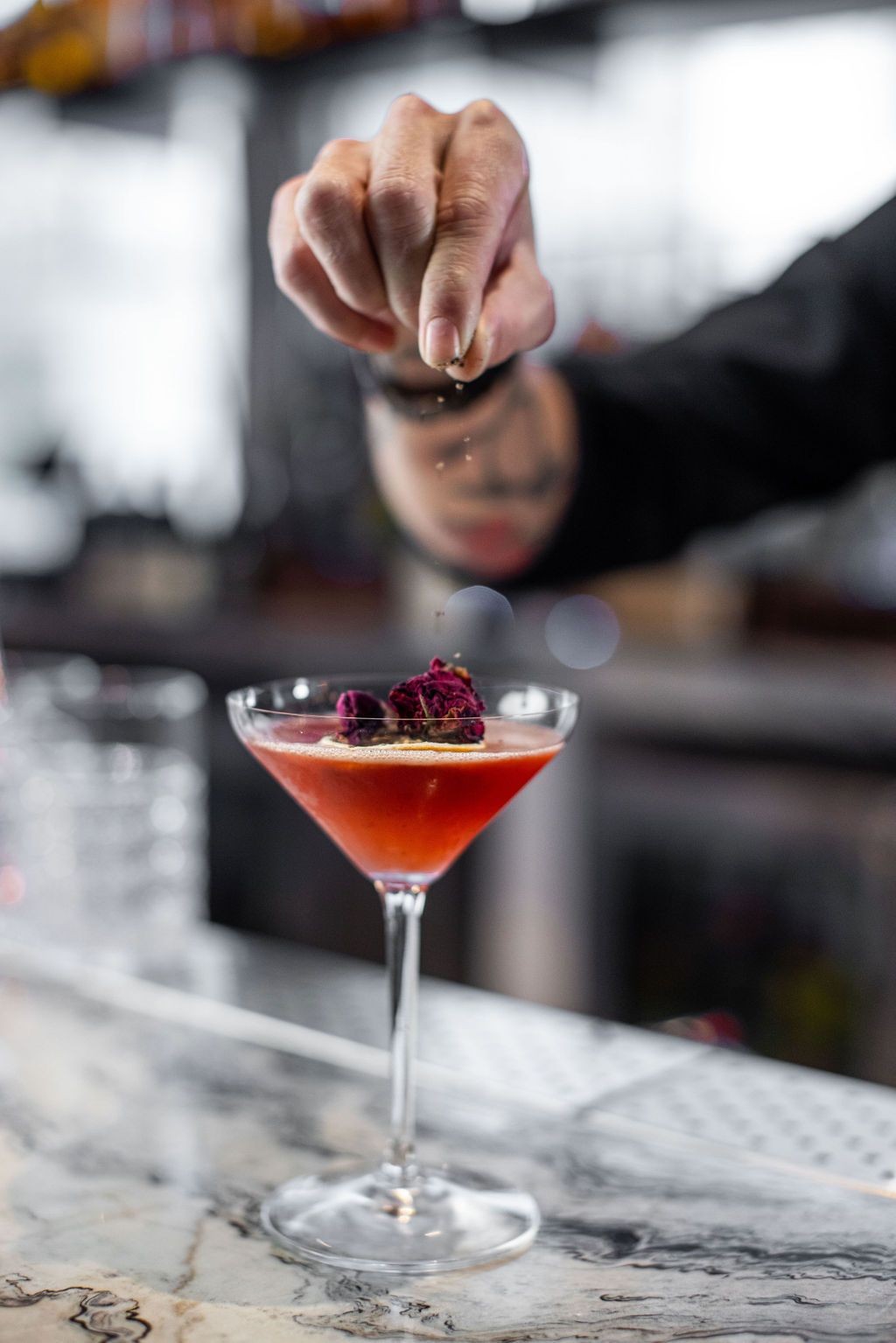 dropping rose petal garnish onto a cocktail in a martini glass